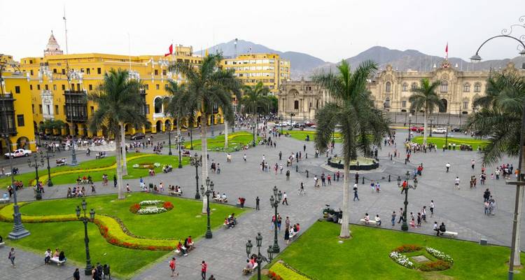 A bustling city square with historical buildings and palm trees.