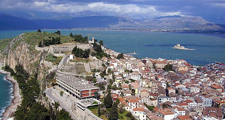 Ciudad de Nafplio con una fortaleza con vista al océano en un día nublado.