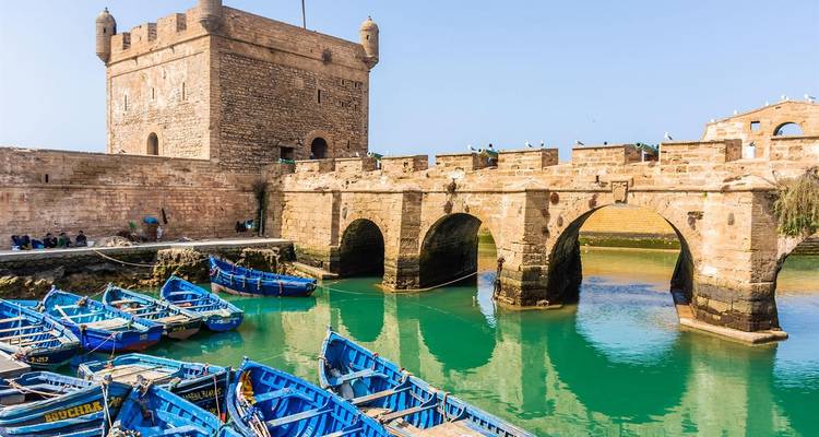 Antigua fortaleza de piedra junto al agua con barcos azules en Essaouira, Marruecos.