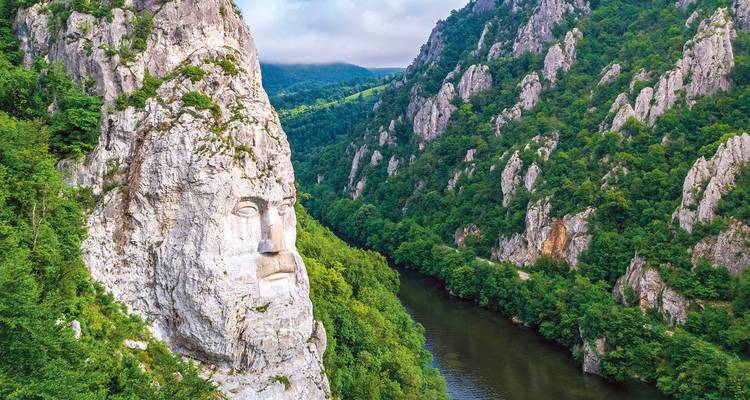 Gran escultura de rostro tallada en un acantilado rocoso sobre un río verde.