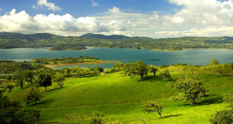 Vue panoramique d'un grand lac entouré de collines verdoyantes et de montagnes.