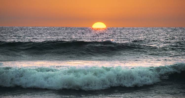 Coucher de soleil sur l'océan avec des vagues qui roulent doucement vers le rivage.