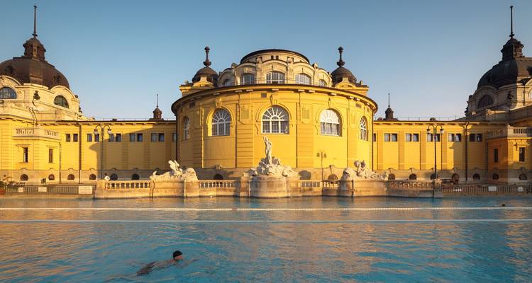 Bain thermal Széchenyi de style Néo-Baroque jaune éclatant avec un nageur solitaire profitant de la piscine extérieure fumante à l'aube.