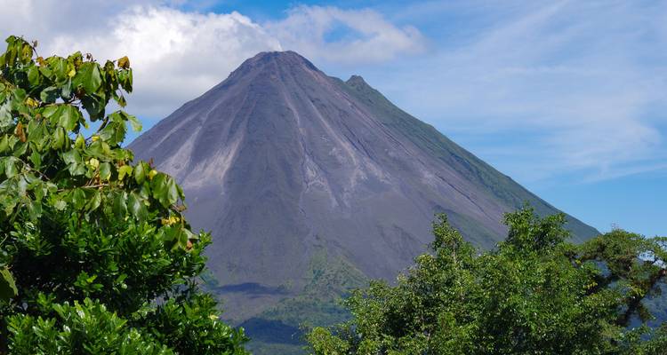 El volcán Arenal de forma cónica se eleva sobre exuberante vegetación tropical bajo un cielo azul