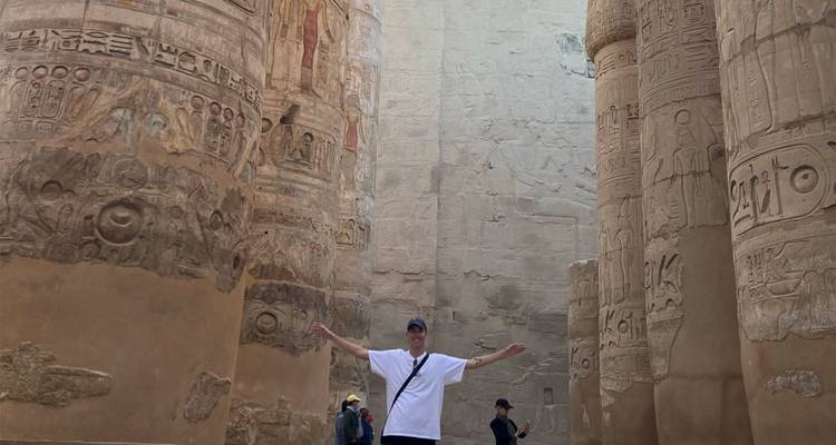 Tourist spreads arms among towering hieroglyph-covered pillars in Karnak Temple.
