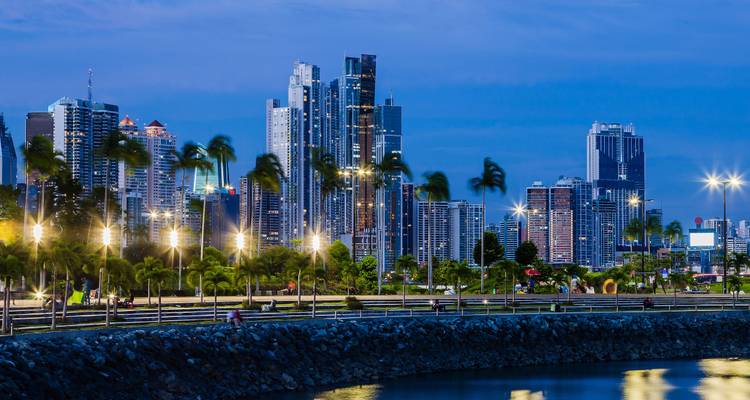 Horizonte moderno de la Ciudad de Panamá iluminado al atardecer con palmeras mecidas por el viento a lo largo del paseo marítimo.