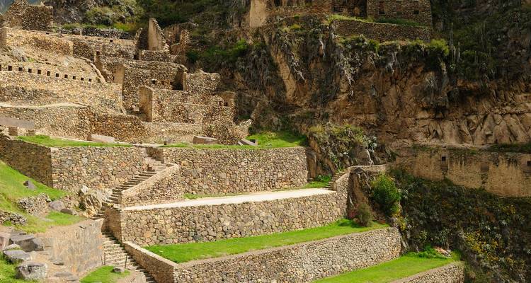 Steinterrassen und verfallene Strukturen von Ollantaytambo, die sich an einem grünen Berghang erheben.
