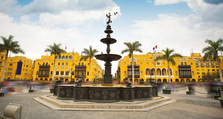 Historischer Plaza de Armas in Lima mit verziertem zentralem Brunnen, gelben Kolonialgebäuden und unscharfen Menschenmengen.