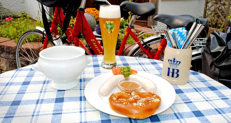 Traditionele Beierse snack van krakeling, witte worstjes en tarwebier naast een geparkeerde fiets