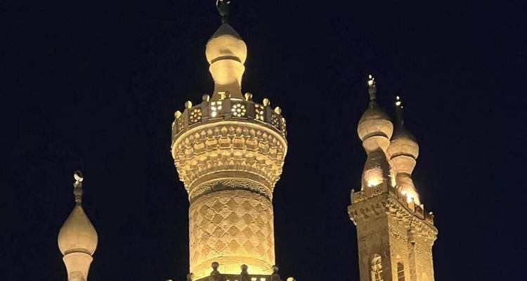 Minaretes iluminados por la noche contra un cielo oscuro.