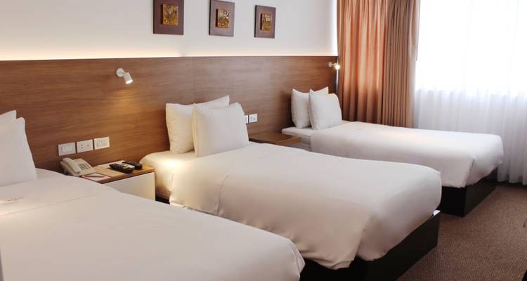 Habitación de hotel con tres camas bien hechas e iluminación cálida.