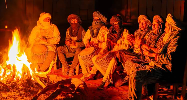 Un groupe de musiciens portant des tenues traditionnelles jouant du tambour autour d'un feu de camp.