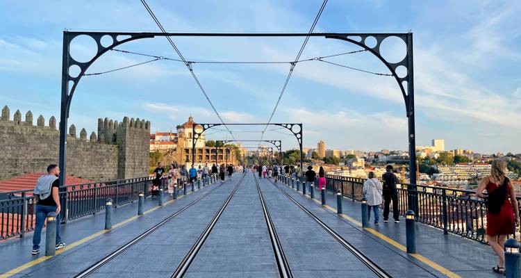 Vista a lo largo de la cubierta superior del Puente Dom Luís I con vías de tranvía, peatones y el horizonte de Oporto a la luz del atardecer.
