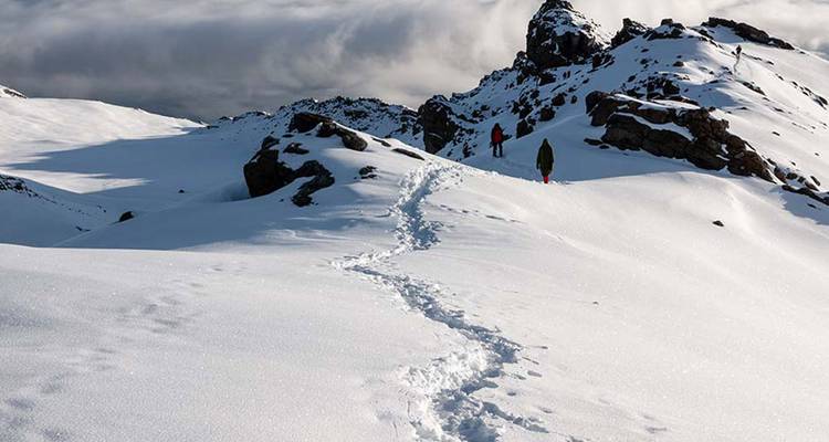 Snowy terrain with two hikers trekking through the snow.