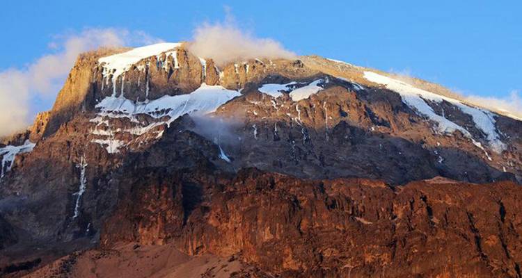 Detailed view of snow-covered mountain cliff with warm sunlight.
