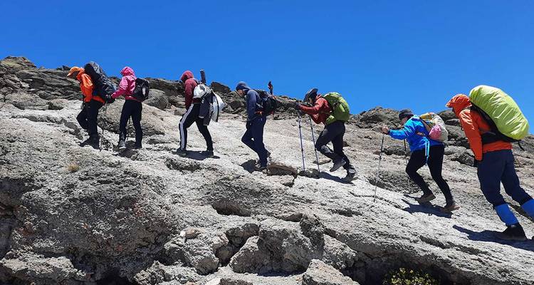Group of hikers ascending a rocky mountain trail under clear skies.
