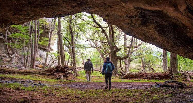 Twee wandelaars staan onder een grotsoverhanging en kijken uit over een groene bosrijke vallei