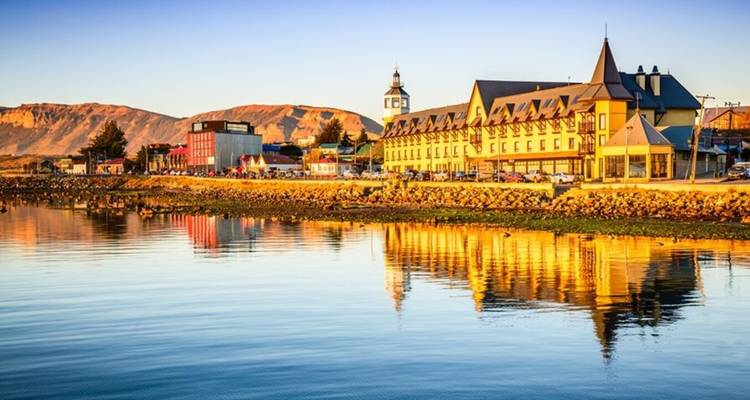 Kleurrijke waterkantwgebouwen van Puerto Natales die weerspiegelen in rustig water tijdens het gouden uur