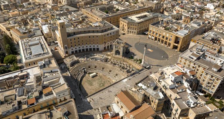 Drone-opname boven het Romeinse amfitheater van Lecce en de honing-geel gekleurde barokke gebouwen in het stadscentrum.