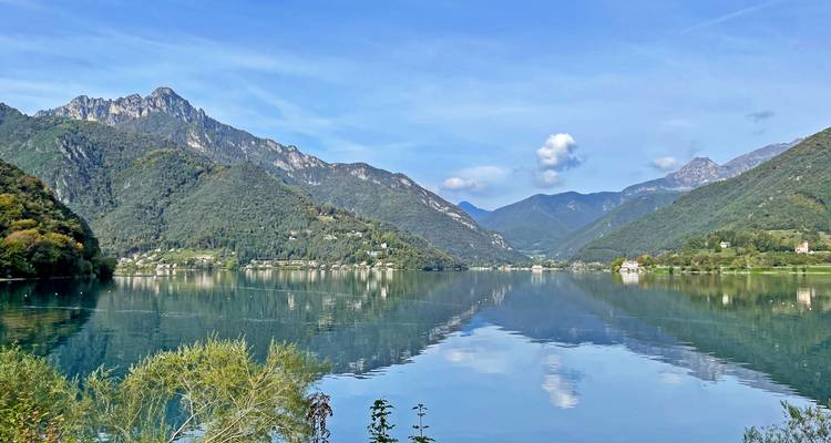 Lac d'un calme parfait entouré de montagnes boisées sous un ciel bleu éclatant parsemé de nuages épars.