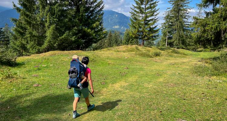 Un niño cargando una mochila de senderismo caminando por un prado exuberante.