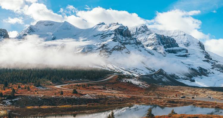 Route de montagne pittoresque avec des sommets enneigés et des nuages.