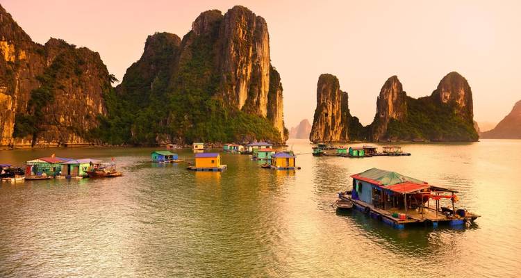 Des maisons de pêche flottantes parsèment les eaux émeraude sous les piliers calcaires de la baie d'Halong au crépuscule.