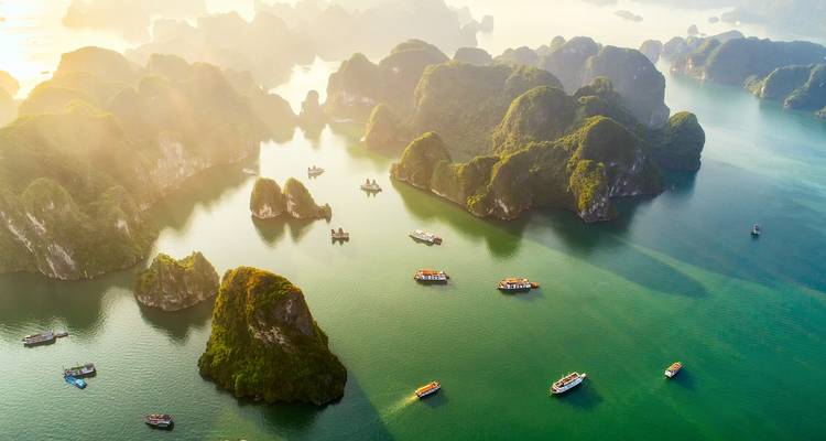 Vue aérienne des eaux émeraude parsemées d'îlots calcaires couverts de jungle et de bateaux touristiques dans la baie d'Halong.