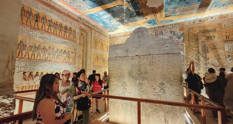Des touristes à l'intérieur d'une tombe avec des hiéroglyphes aux couleurs vives.