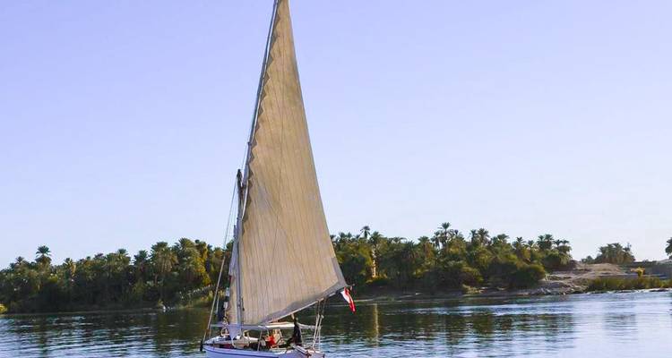 Pequeño velero en un río tranquilo con un fondo tropical.