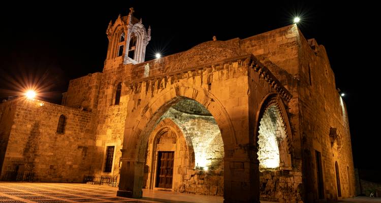 A historic stone church glows under dramatic night lighting, showcasing ornate arches and a tall bell tower.