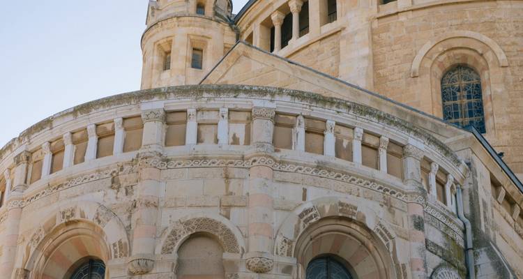 Close-up of a Romanesque stone basilica showing rounded apses, striped stonework and arched windows against a pale sky.