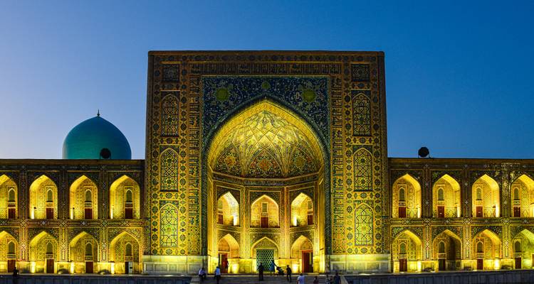 Un gran edificio arquitectónico con azulejos azules vibrantes, iluminado por la noche.