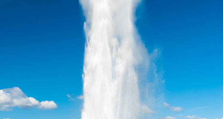 Vertikaler Wasserstrahl eines Geysirs schießt in einen wolkenlosen blauen Himmel in Island.