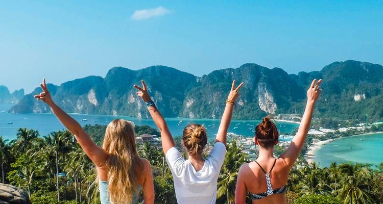 Trois femmes avec les mains levées en signe de paix surplombant une baie magnifique remplie d'îles calcaires.