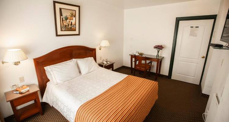 Intérieur d'une chambre d'hôtel avec un lit double, un petit bureau et une chaise.