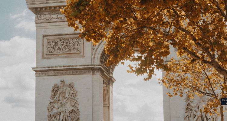 Close-up van de Arc de Triomphe omlijst door herfstbladeren onder een zachte hemel