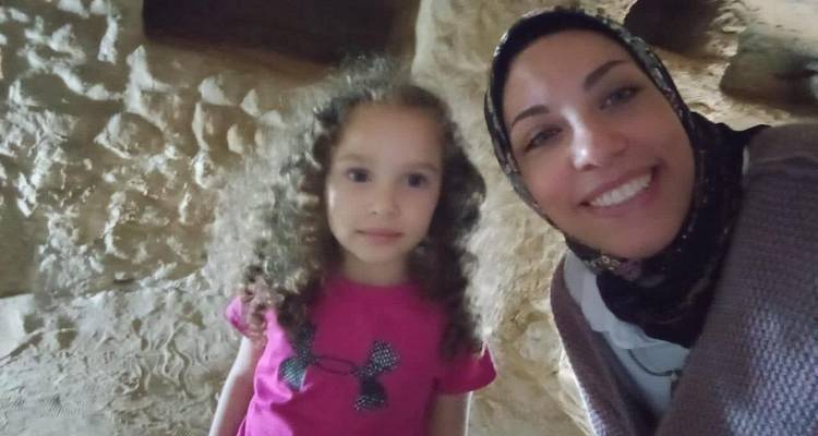 Una mujer y una niña sonriendo dentro de una cueva antigua con paredes de piedra ásperas.
