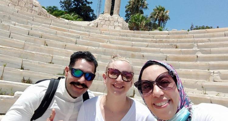 Tres personas posando y sonriendo en escalones de piedra escalonados con follaje verde cerca.