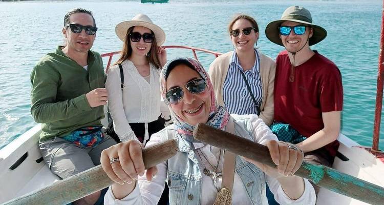 Un grupo de cinco personas en un barco disfrutando del clima soleado con agua en el fondo.