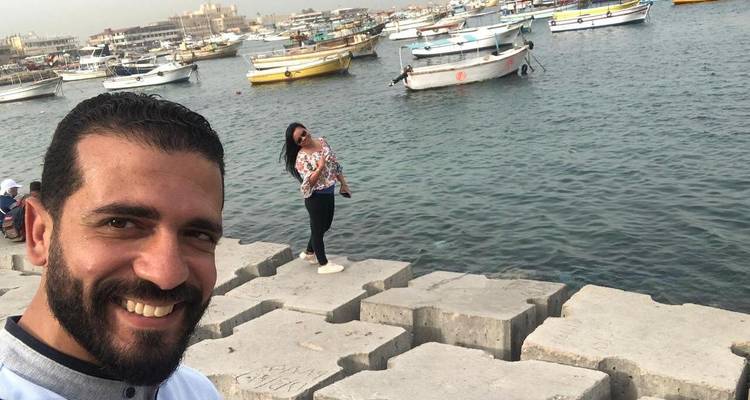 Una selfie junto al mar con barcos en el fondo.