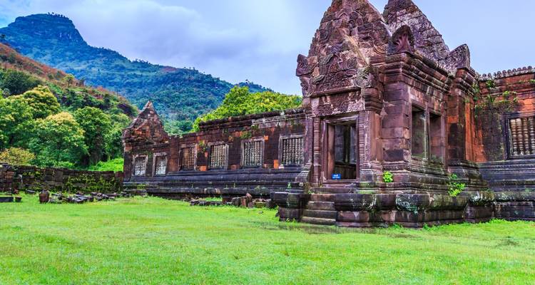 Ruines du temple antique en grès de Wat Phou sur fond de montagnes couvertes de jungle et de pelouse ouverte.