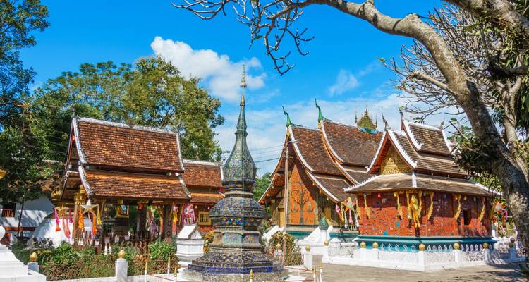 Complexe de temple bouddhiste orné avec des toits de tuiles colorées et un stupa de mosaïque central sous un ciel bleu éclatant.