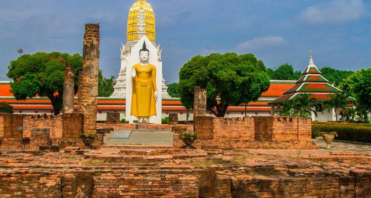 Statue de Bouddha debout dans des ruines historiques en brique encadrée par des arbres luxuriants