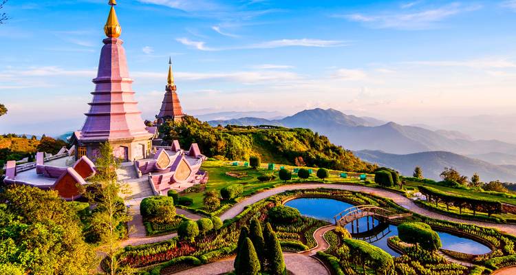 Estupas reales gemelas rodeadas de jardines cuidados en la cima de una cresta montañosa con vistas panorámicas del norte de Tailandia.