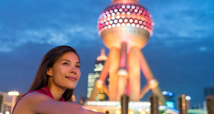 Person smiling with Shanghai's Oriental Pearl Tower lit up at night.