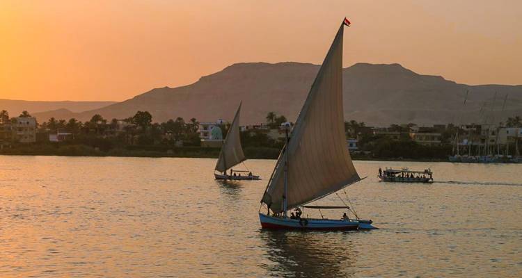 Veleros en un río durante el atardecer con una cordillera al fondo.