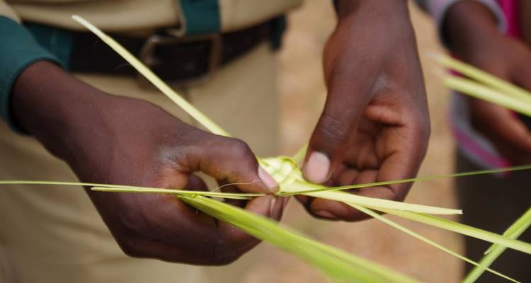 Primer plano de manos tejiendo hojas de palma.