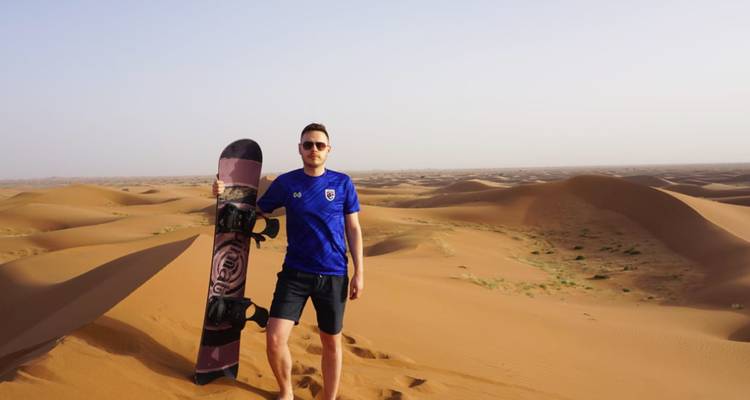 Persona sosteniendo una tabla de arena parada en un desierto