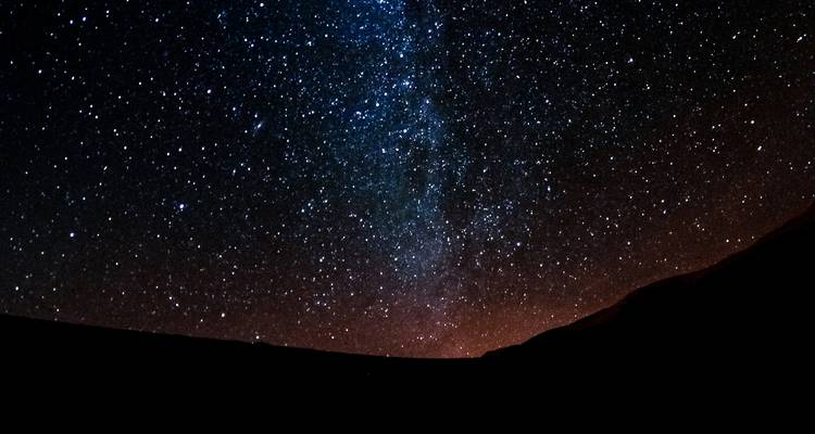 Cielo nocturno estrellado sobre la silueta de dunas de arena.